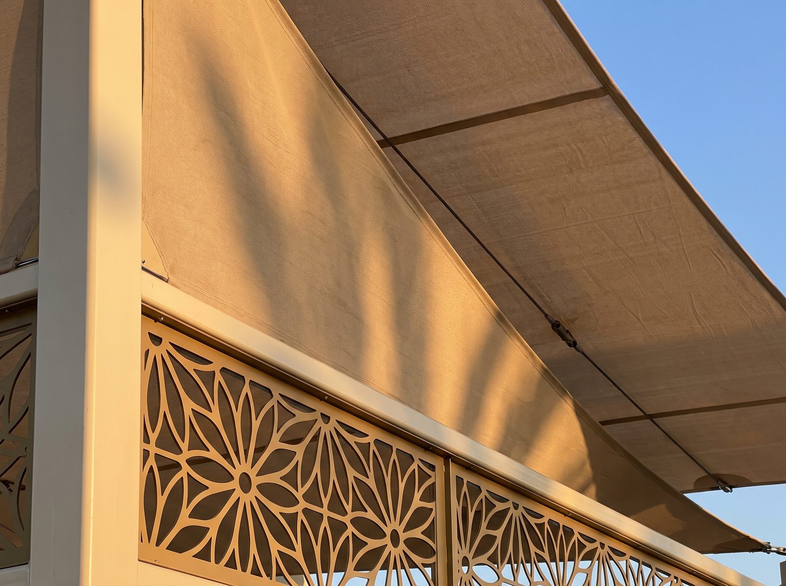 مظلة قماشية كابولي بلون بيج مع لوحة زخرفية معدنية مقصوصة بالليزر بلون ذهبي وعمود دعم متين